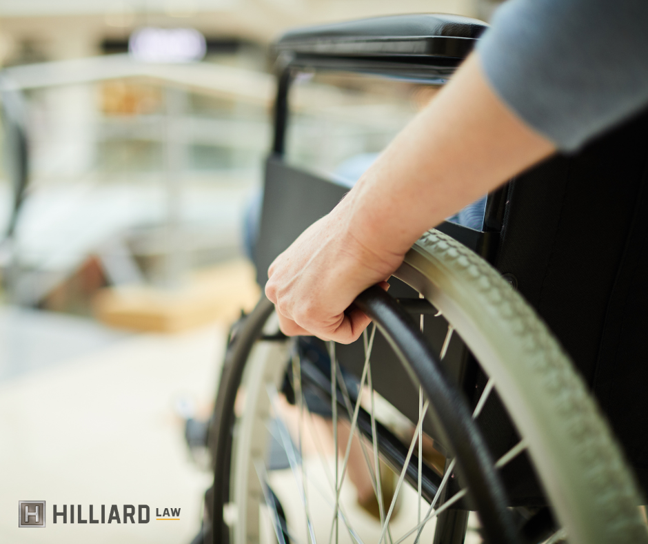 Image shows the lower left side of a wheelchair. A person's hands are on the wheel, indicating they are in motion.