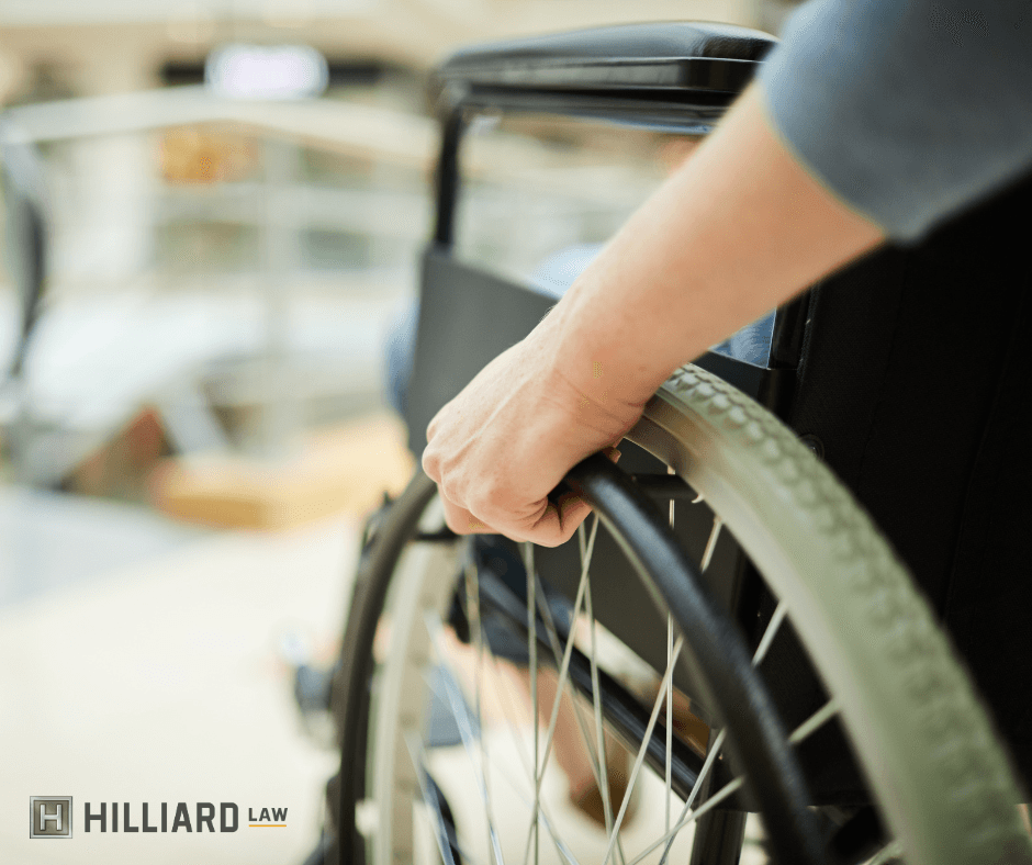 Image shows the lower left side of a wheelchair. A person's hands are on the wheel, indicating they are in motion.