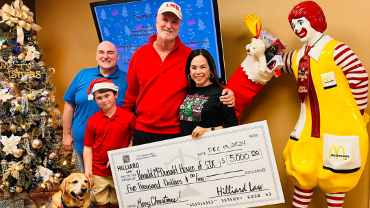 Image of Bob, Catherine & Del Hilliard, pictured with Cory Boemer, and Duke, a service dog. They are holding a large check, standing next to a statue of Ronald McDonald.