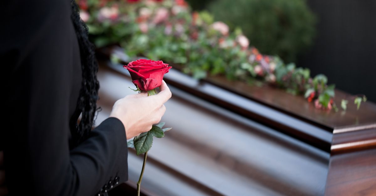 holding rose in front of a casket at a funeral
