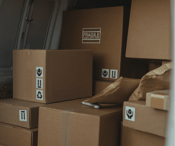 Image shows cardboard boxes stacked in the back of a delivery van.