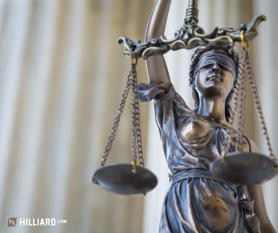 Image of a bronzed scales of justice. In the background are courthouse pillars. There is a hilliard law logo in the lower left hand corner.