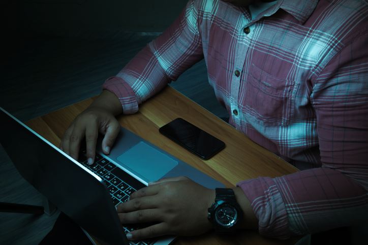 A man is sitting on a laptop in a dark room with lights shining down on it.internet concept addiction.topview. stock photo