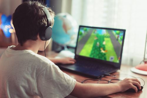 Little dependent gamer boy playing on laptop at home