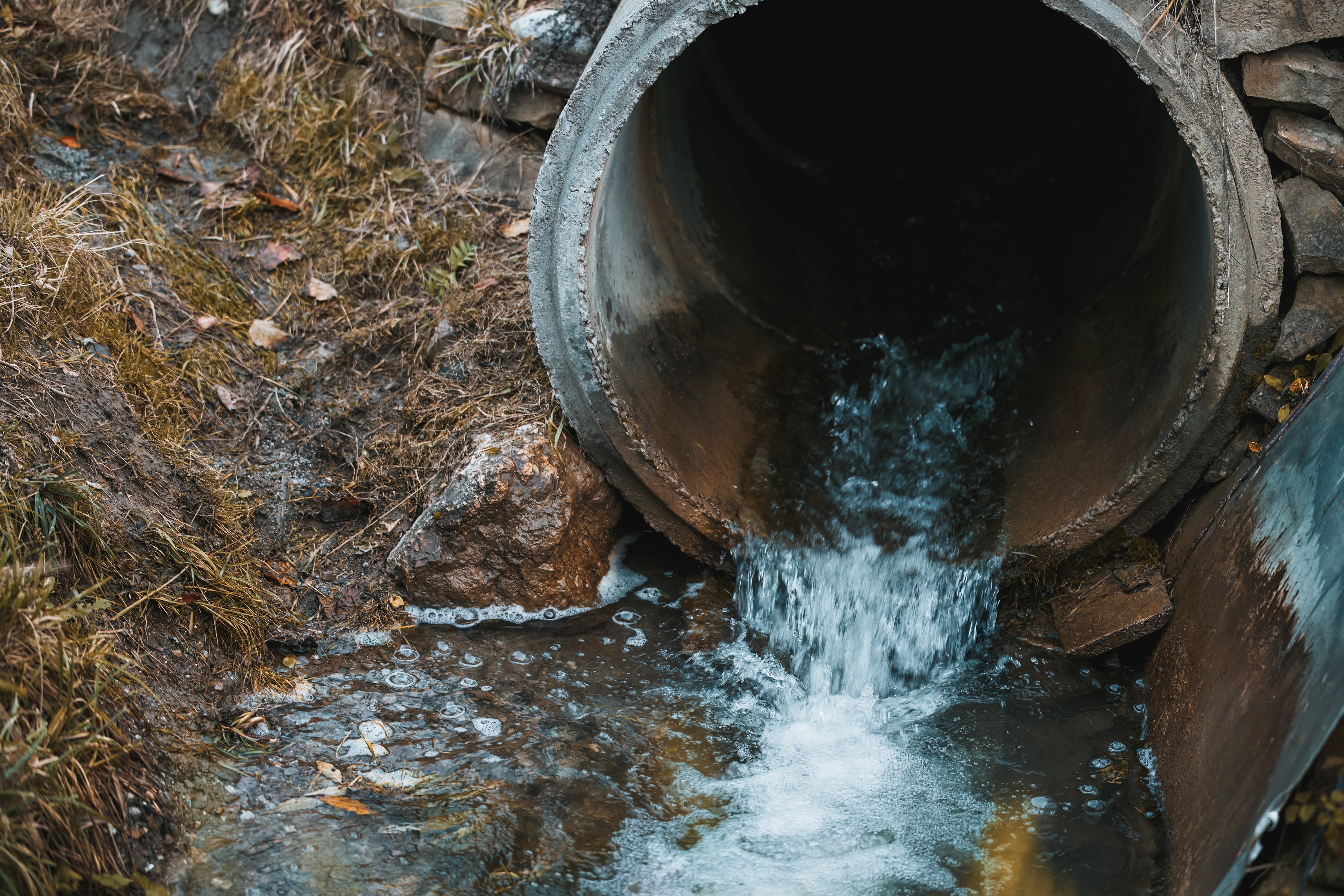 A sewage pipe drains toxic wastewater into a river, causing environmental pollution and ecological damage.