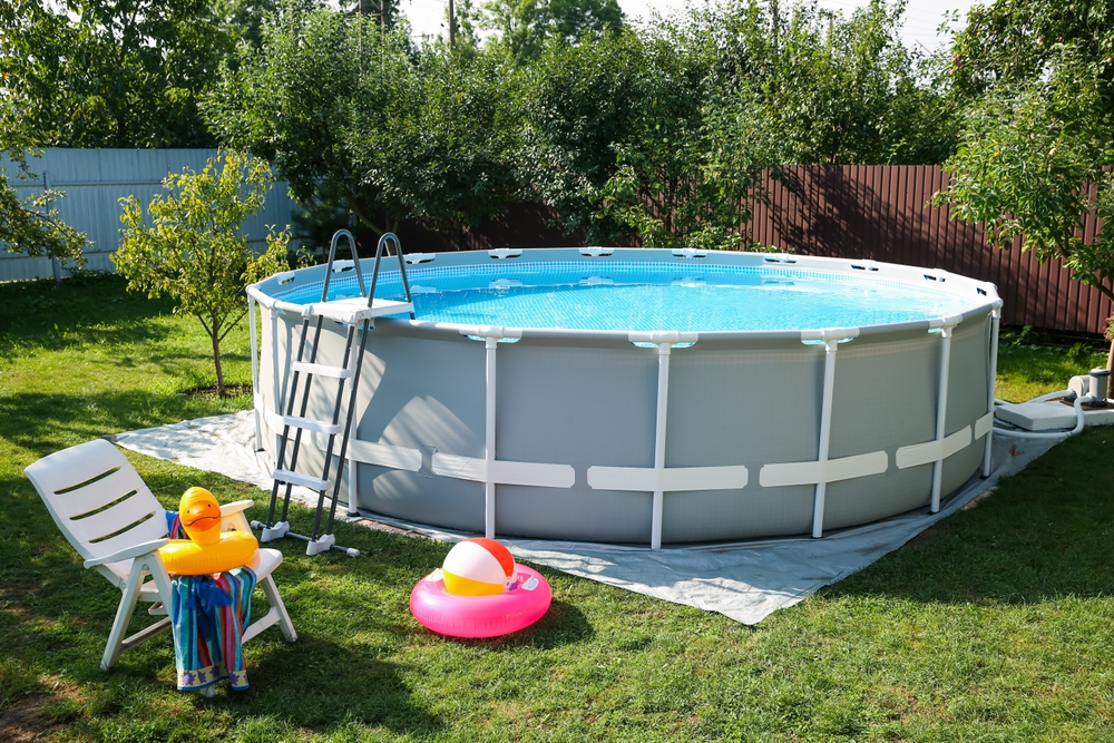 Above ground swimming pool, folding chair, towel, inflatable rings and ball in backyard