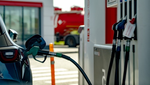 Blue car at gas station pump. Red fire truck parked nearby. Modern fuel station with multiple nozzles. in the scene. Ideal for energy, transportation, or daily routines