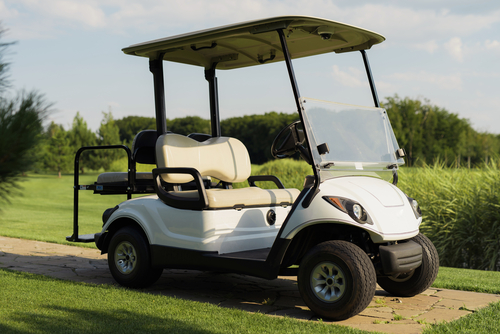 A white golf car stands on a stone path against the backdrop of a golf course